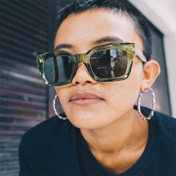 A girl wearing the Anna Green Sunglasses – Unisex square-frame sunglasses with forest green frame and green UV400 lenses, medium-large fit, made from recycled plastic.
