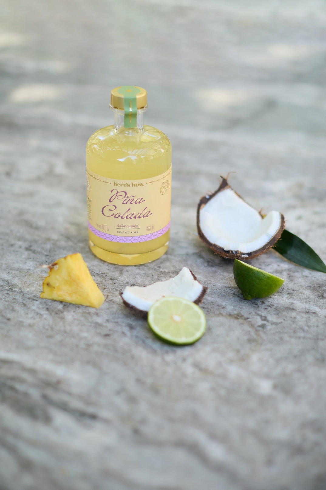 Bottle of Cura Corailada rum with coconuts, pineapple, and lime on a textured surface