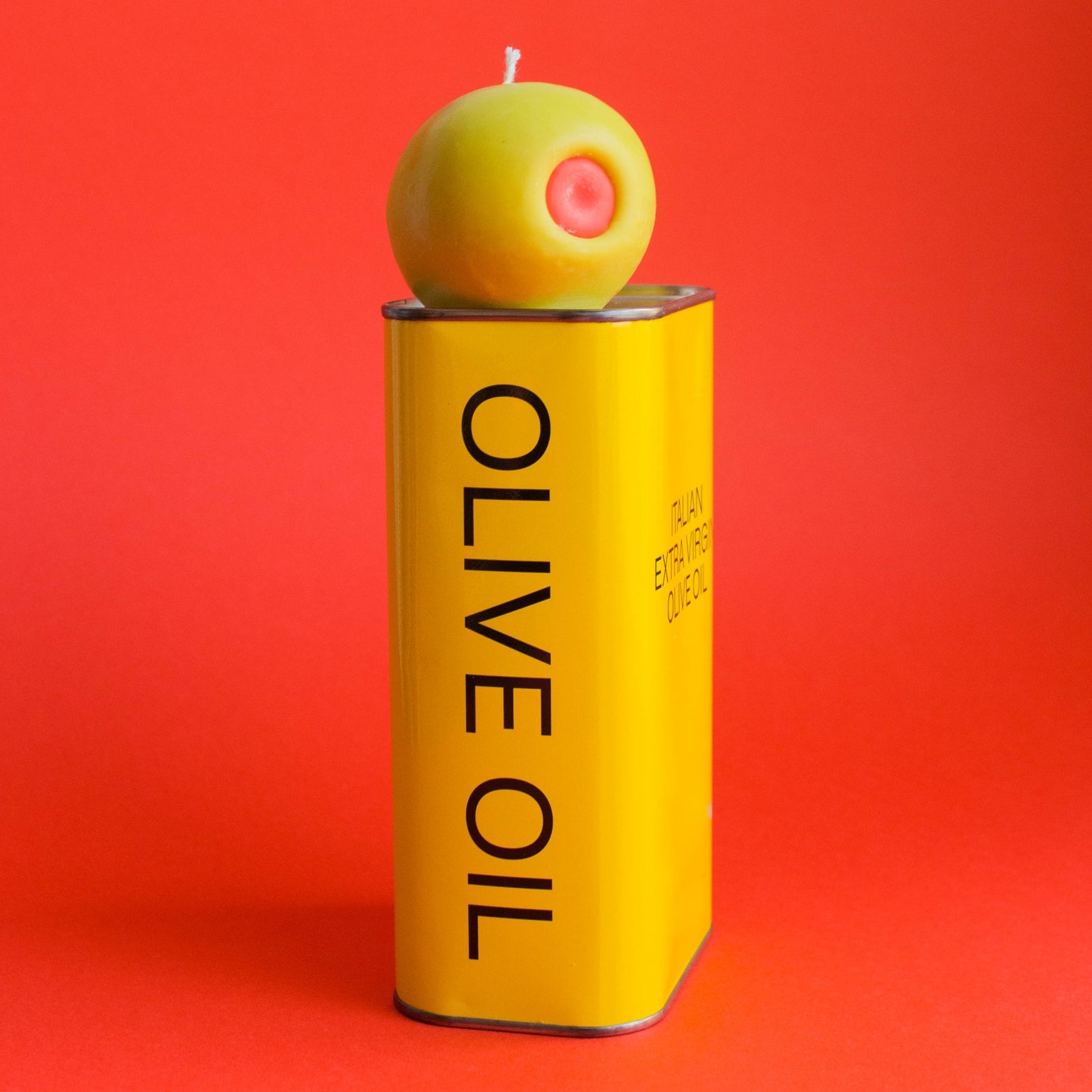  Olive oil can with a green olive candle on top against a red background