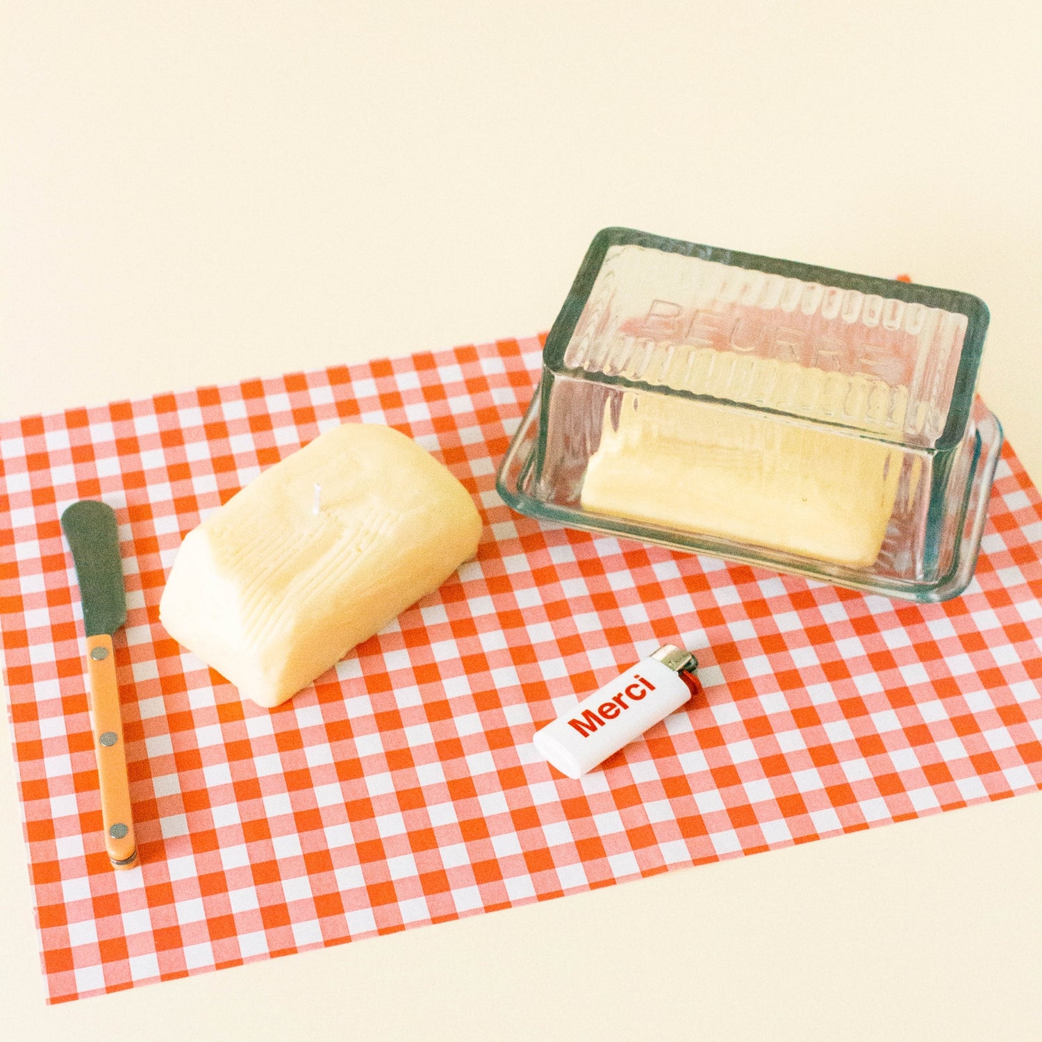 Butter candle, knife, and glass container on a red and white checkered tablecloth