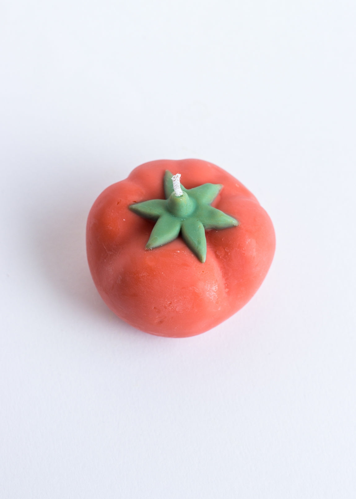 Red candle tomato-shaped with green stem on a white background