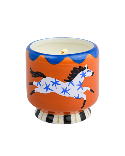 “A Dopo Horse Soy Wax Candle in hand-painted ceramic vessel with white horse and blue motif on orange background, displayed on white backdrop.”