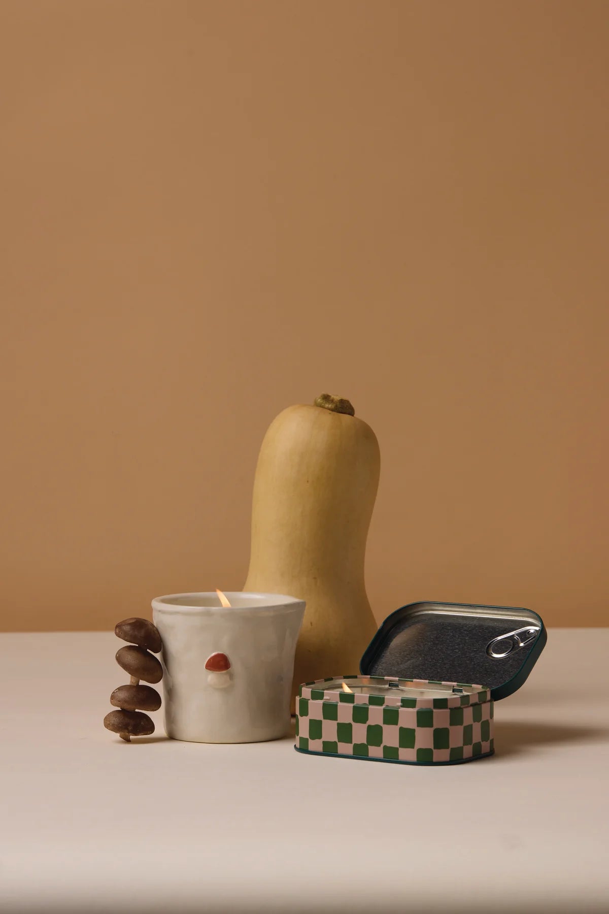 Butternut squash, ceramic mushroom candle, tin mushroom candle on a beige background