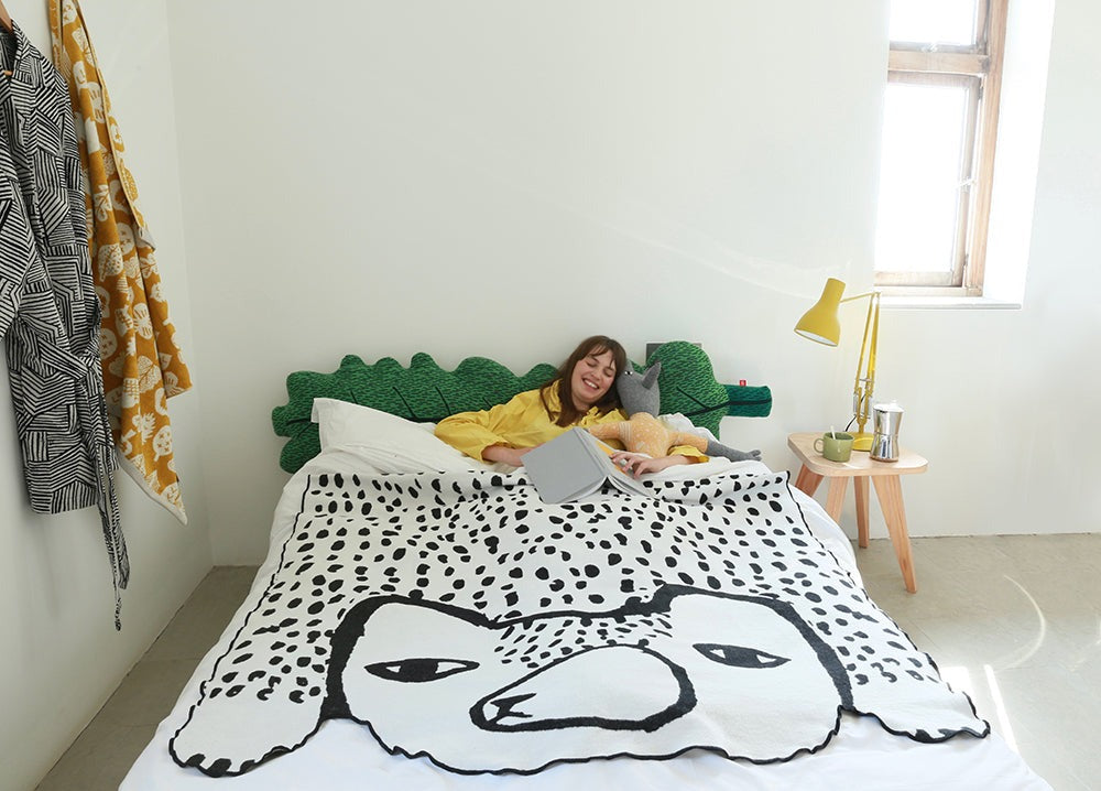 Person lying on a bed with a bear shaped blanket in a bright room