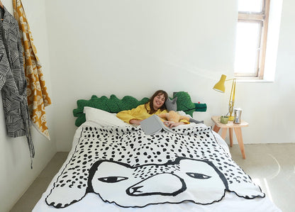 Person lying on a bed with a bear shaped blanket in a bright room