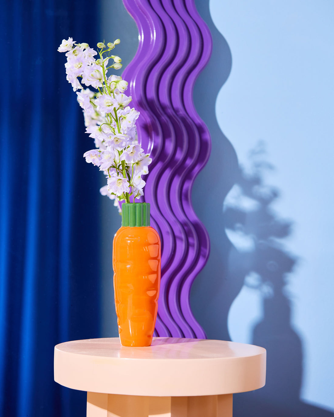 Carrot-shaped vase with flowers on a round table against a blue and purple gradient background