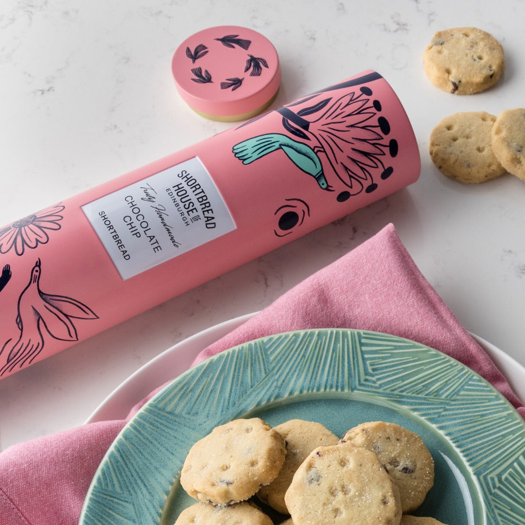 Pink tube of chocolate chip shortbread cookies with cookies on a plate and surface