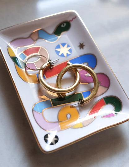Compact ceramic trinket dish with hand-painted rainbow snake design and 10k gold detailing, holding earrings and small jewelry, ideal for keys or other essentials, presented in an eco-friendly gift box.