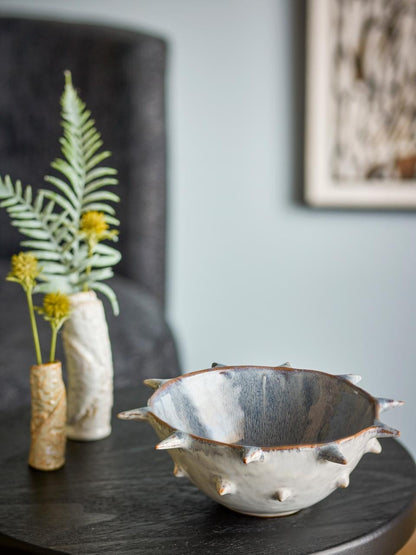 Edie Ceramic bowl , with a vase of plants in the background.