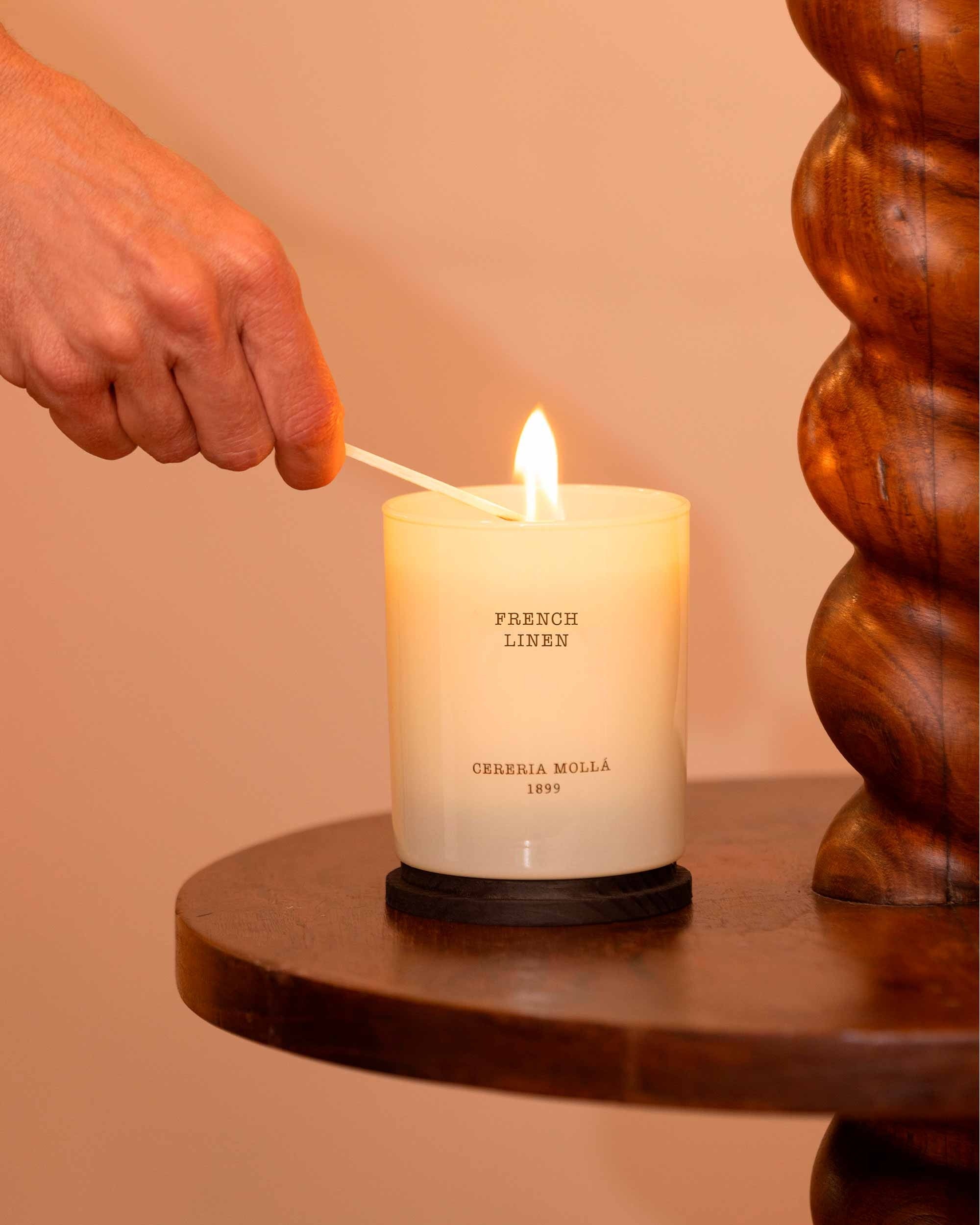 French Linen Candle being lit with a wooden wick trimmer on a wooden surface.