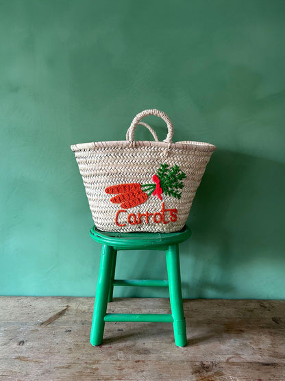 Handwoven palm leaf market basket with embroidered carrot design on a green chair
