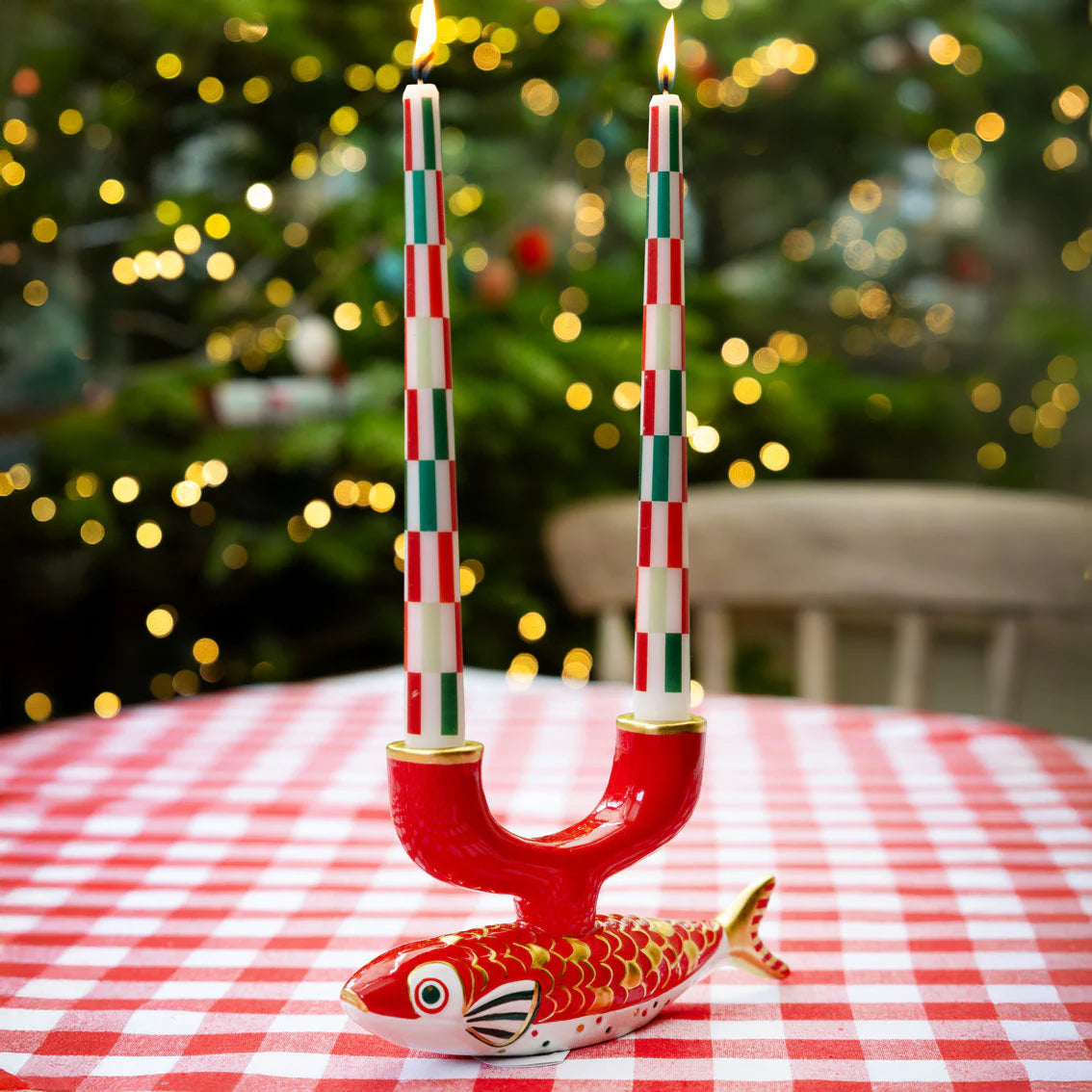 Decorative candle holder shaped like a fish with striped candles on a tablecloth in front of a Christmas tree.