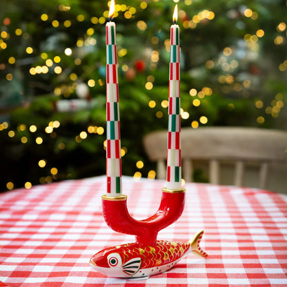Decorative candle holder shaped like a fish with striped candles on a tablecloth in front of a Christmas tree.