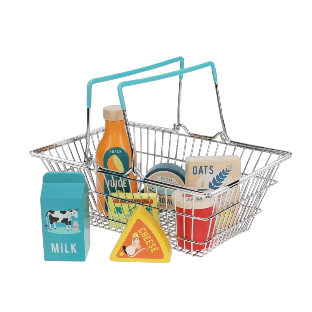 A metal shopping basket with rubberised plastic handles, containing various wooden pretend grocery items like milk carton, triangle cheese, oats, orange juice, and others.