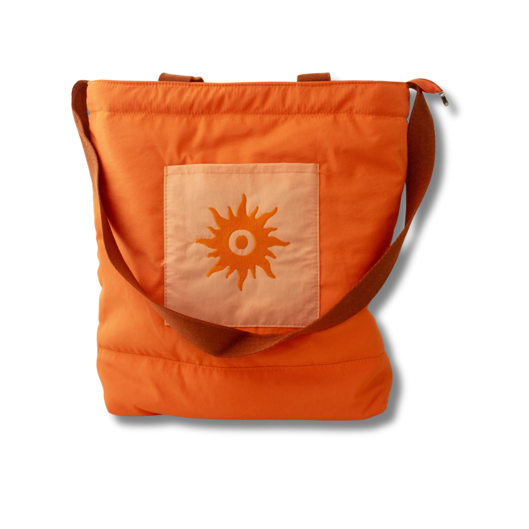 A burnt orange nylon beach tote with a sun pattern, featuring a top handle, a zipper closure, and an embroidered pocket on the front.
