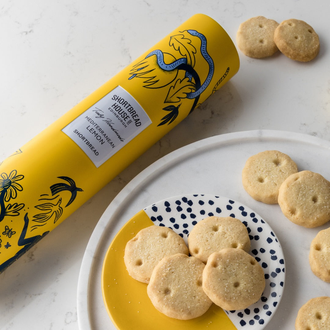 Yellow tube of lemon shortbread cookies on a marble surface with cookies around