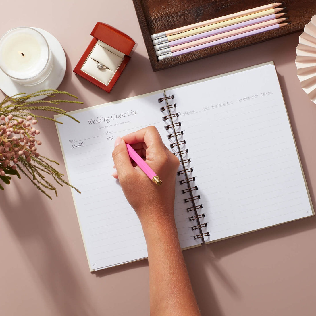 Hand writing in awedding planner notebook with a pink pen, on a pink surface.