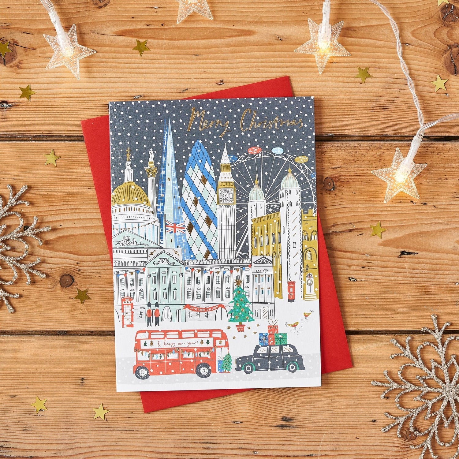 Gold Foiled Christmas Card featuring London landmarks in snow: Big Ben, Tower Bridge, Gherkin, London Eye; on a wooden surface