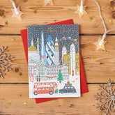 Gold Foiled Christmas Card featuring London landmarks in snow: Big Ben, Tower Bridge, Gherkin, London Eye; on a wooden surface