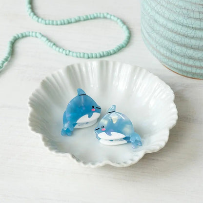 Two blue dolphin hair clips on a white shell with a light blue beaded necklace in the background.
