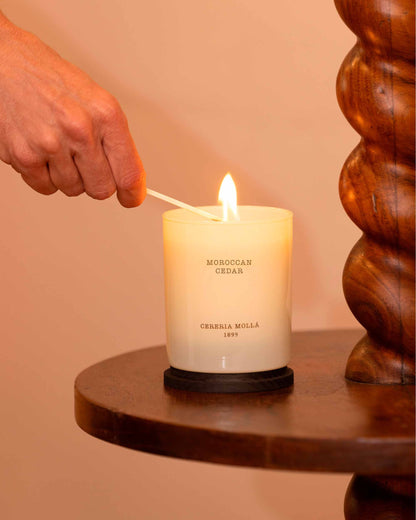 Moroccan Cedar being lit with a wooden wick trimmer on a wooden surface.