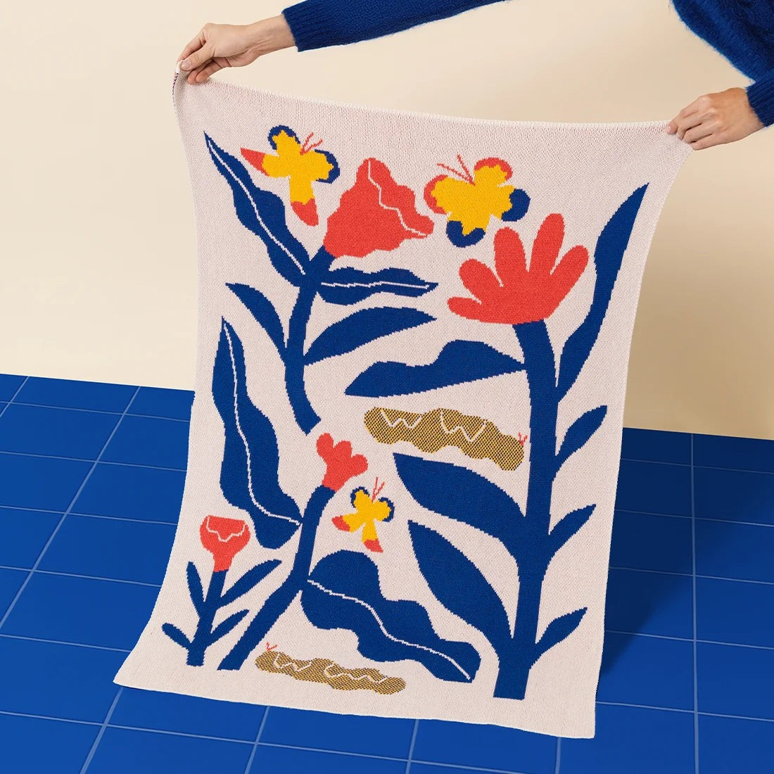 A person holding with two hands the Papillons Mini Blanket 30x40 inches, designed byAmélie Lehoux, made from 50% cotton and 50% recycled polyester, soft and eco-friendly, made in USA. 