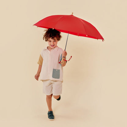 Child holding a red umbrella on a beige background