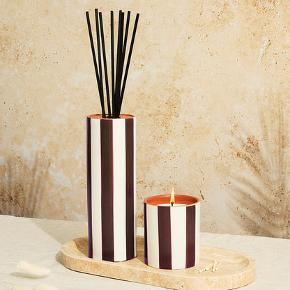 Striped diffuser and candle set on a marble surface with a beige stone background
