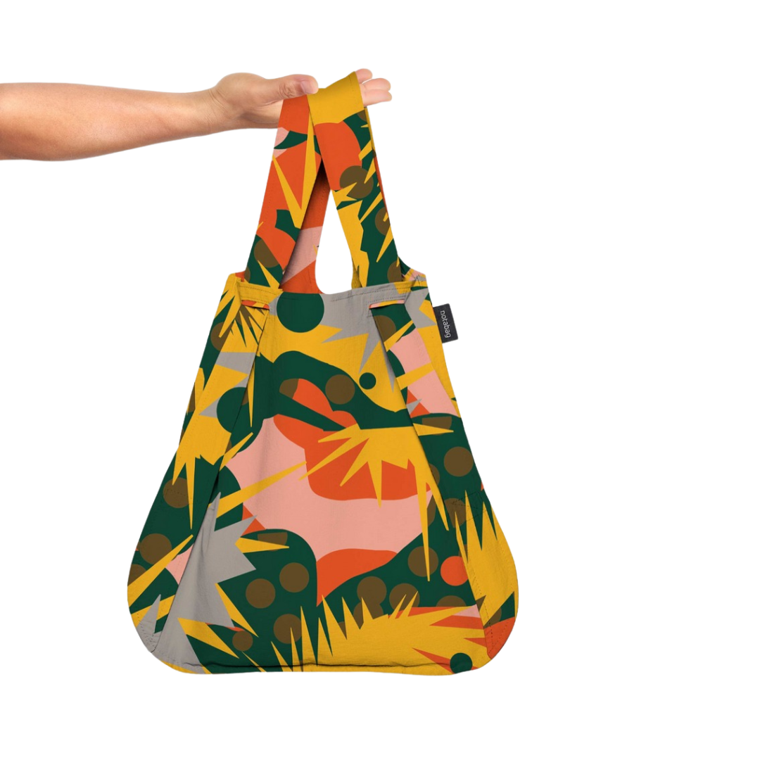 A hand holding a multicolored Notabag Spark Bag & Backpack with a floral pattern.