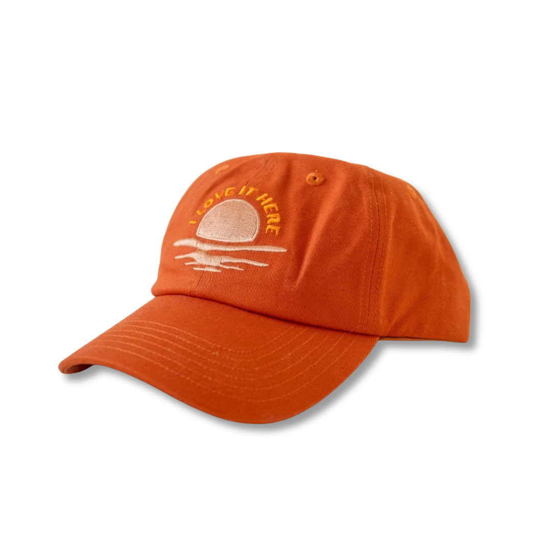 Burnt orange baseball cap with embroidered text &quot;I love it here&quot; and sun and wave design on the front

