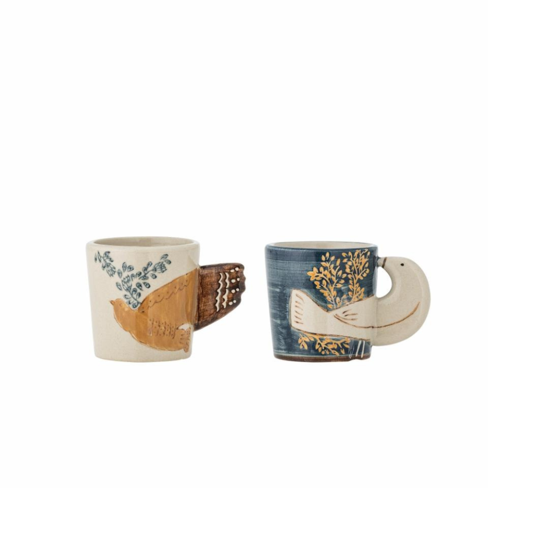 Two Hezha espresso cups on a white background, one in blue and one in nature color, each featuring a delicate bird motif with wings as handles. Hand-decorated, unique ceramic cups ideal for espresso or decorative display.