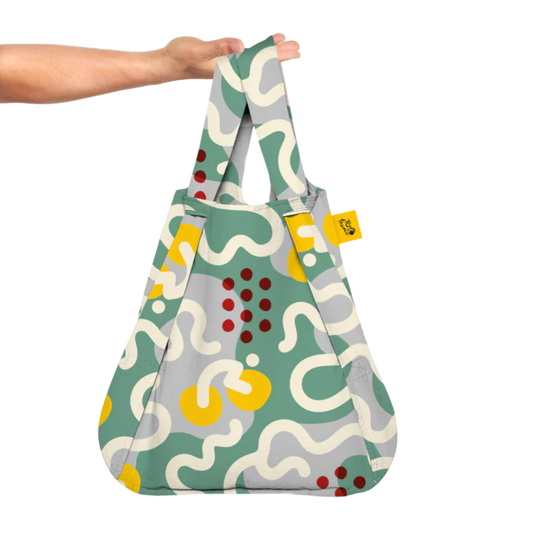 A multicolored geometric patterned bag with handles being held by a hand.