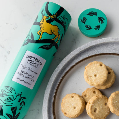 Shortbread cookies on a plate with a teal packaging tube featuring a deer illustration.