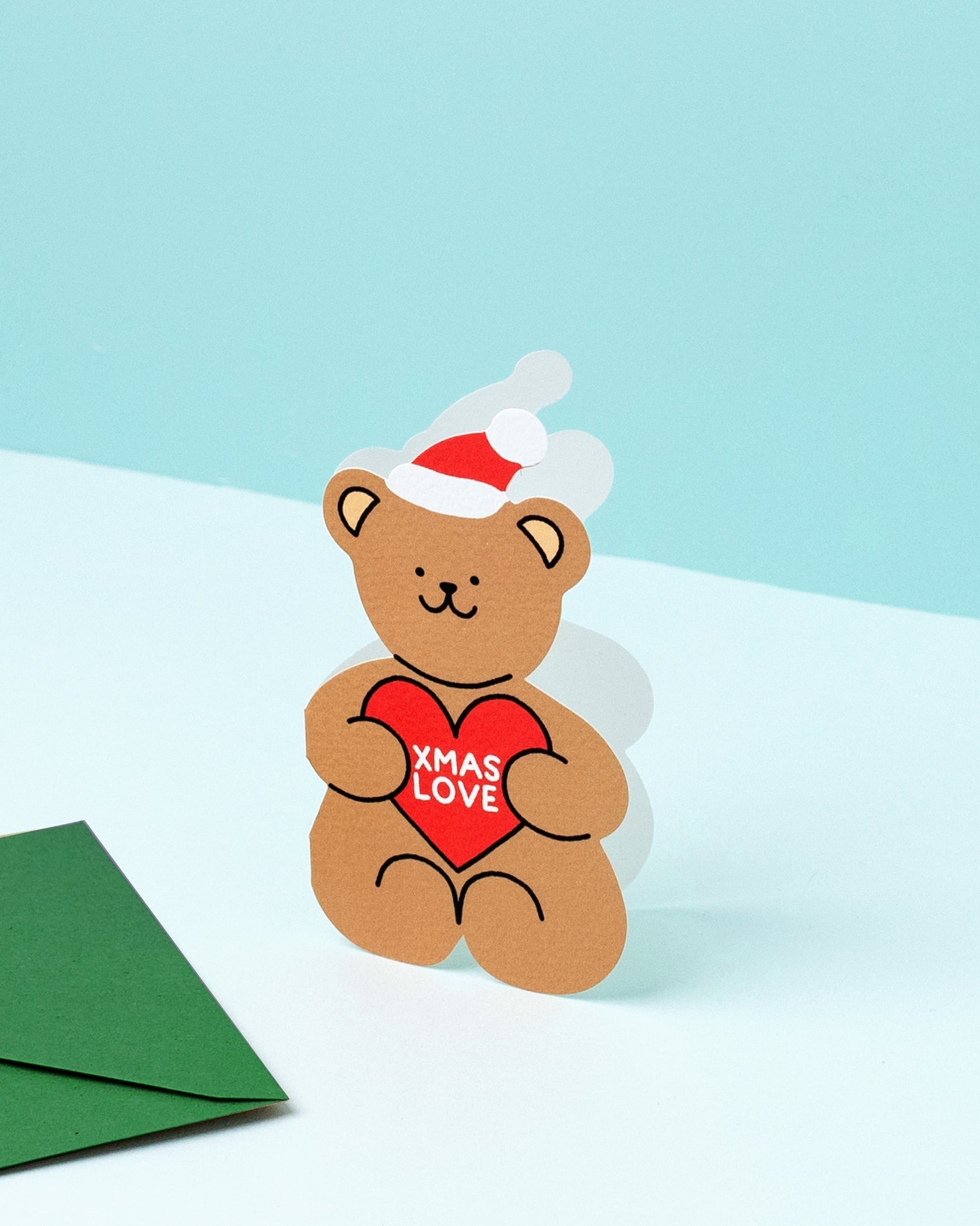 Christmas card bear-shaped with a red heart and 'XMAS LOVE' text on a light blue background