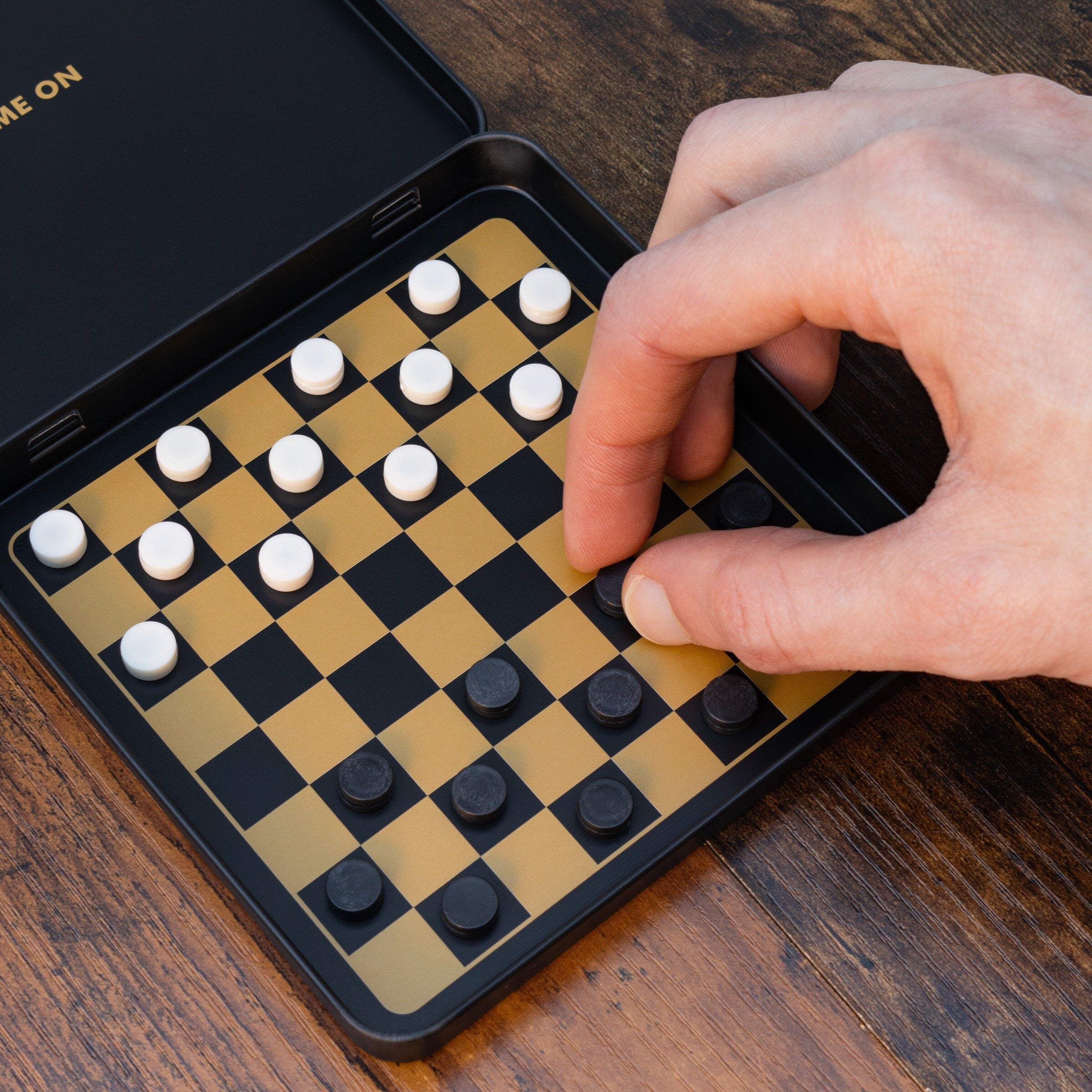 Hand playing checkers on a portable board game set on a wooden surface