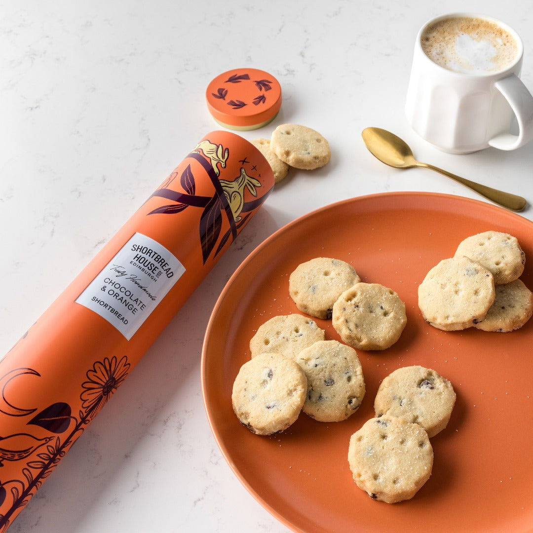 chocolate and orange shortbread cookies on an orange plate with a canister and a cup of coffee.