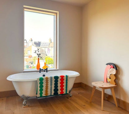 Bathroom with a freestanding bathtub, fizz colorful towel, and a small chair with a decorative backrest.