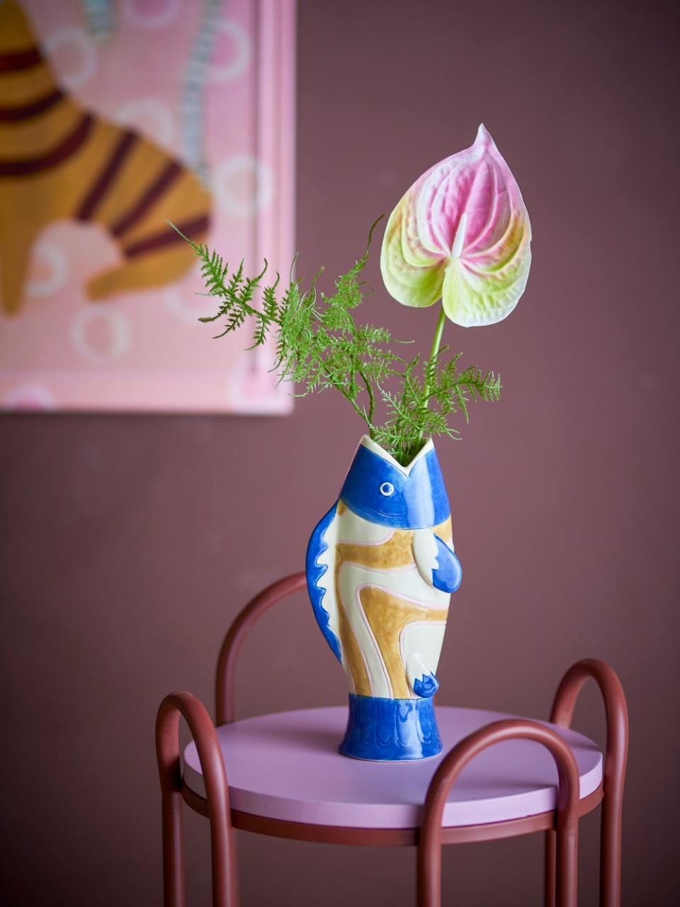 Blue fish-shaped stoneware vase with golden details, displayed on a pink table holding fresh flowers, coastal home décor accent.