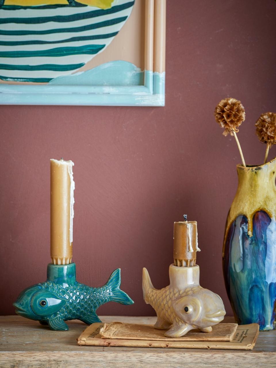 Decorative fish-shaped candle holders on a wooden surface with a framed artwork in the background.