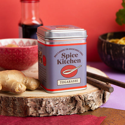 Spice Kitchen Togarashi spice tin on a wooden surface with ginger and bowls in the background.